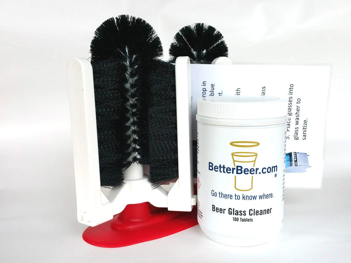 A black bristle glass cleaning brush with a red base stands next to a white container labeled “BetterBeer.com Beer Glass Cleaner, 100 tablets,” with printed instructions partially visible in the background.